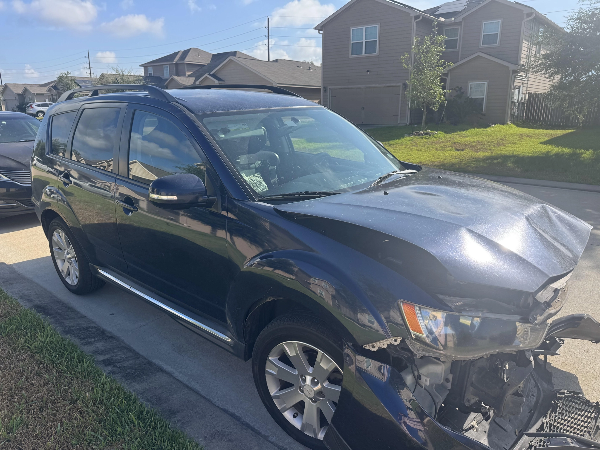 Damaged Mitsubishi Outlander parked in a Houston driveway with front-end collision damage.
